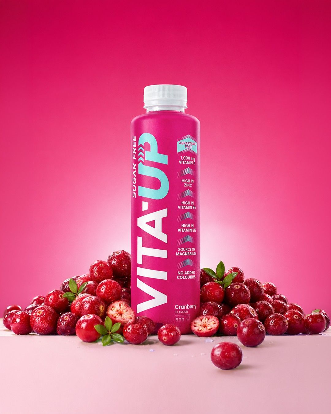 A Cranberry bottle of Vita-Up surrounded by fresh cranberries on a pink backdrop
