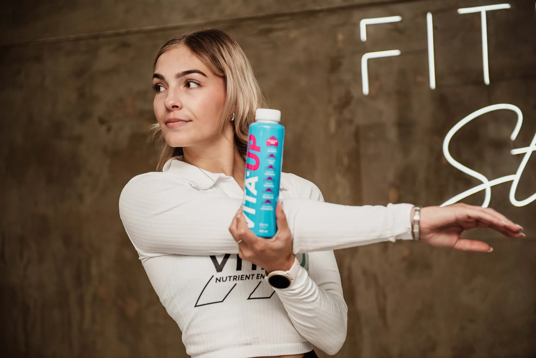Woman stretching while holding a Berry bottle in front of a neon sign